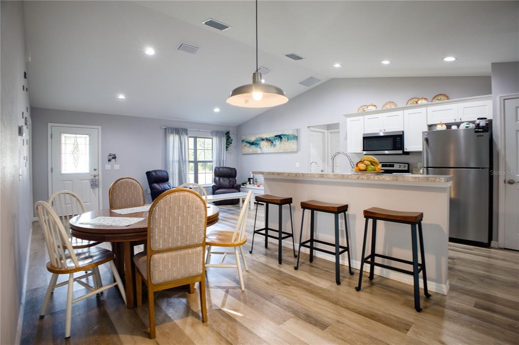 An open-concept kitchen and dining area features wood-look flooring, white cabinetry, and a breakfast bar — 3144 SE 144TH PLACE, SUMMERFIELD, FL