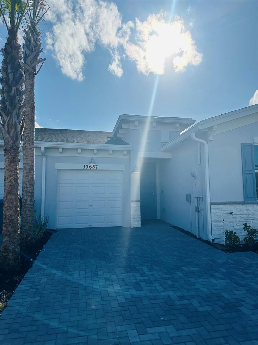 A light blue house exterior features a white garage door, stone accents, and a paved driveway — 13657 Night Sky Place, Delray Beach FL 33484, DELRAY BEACH, FL