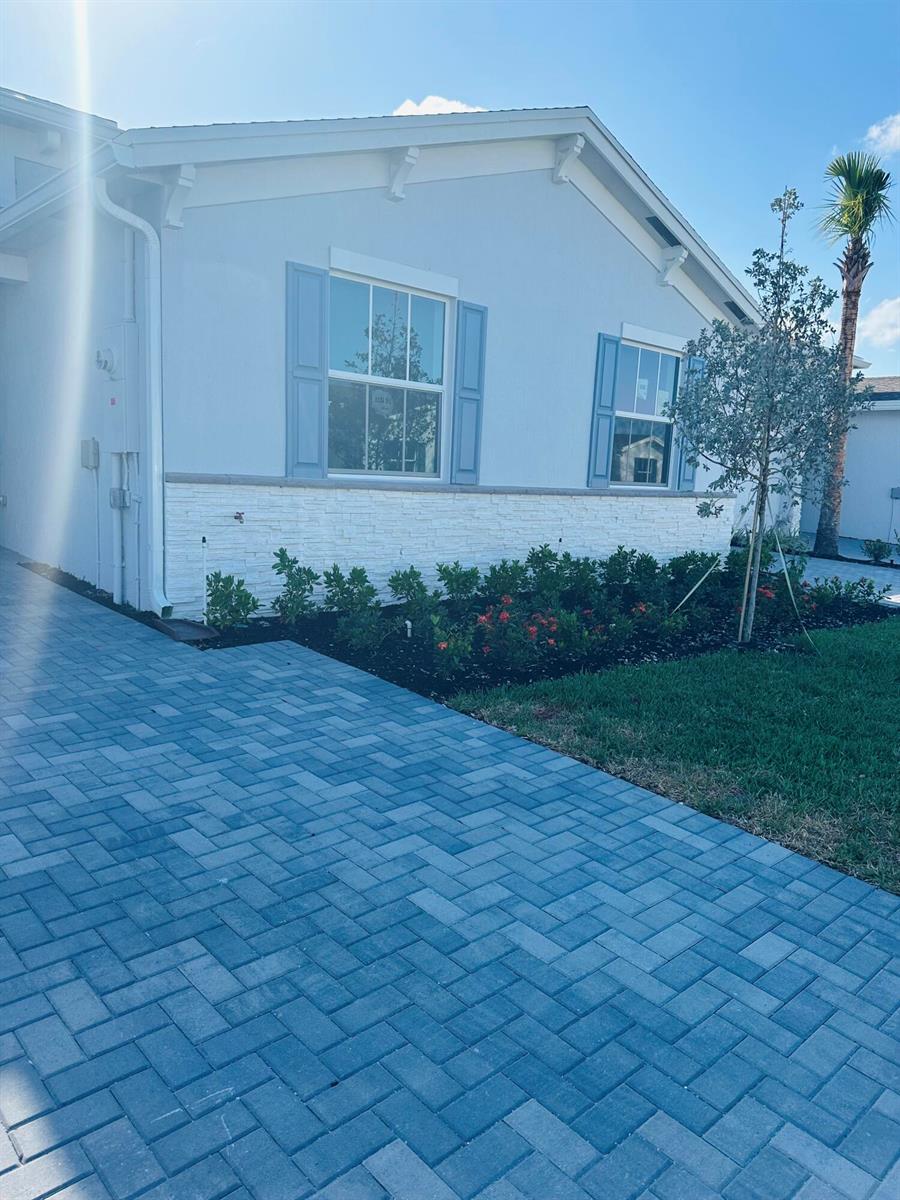 The exterior of a light blue house features white stone siding, blue shutters, and pavers — 13657 Night Sky Place, Delray Beach FL 33484, DELRAY BEACH, FL