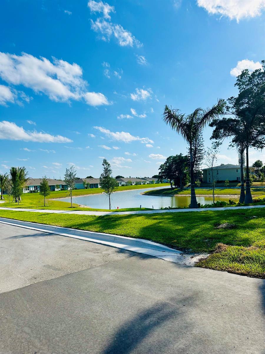 A view of a neighborhood pond surrounded by green lawns, palm trees, and residential houses — 13657 Night Sky Place, Delray Beach FL 33484, DELRAY BEACH, FL