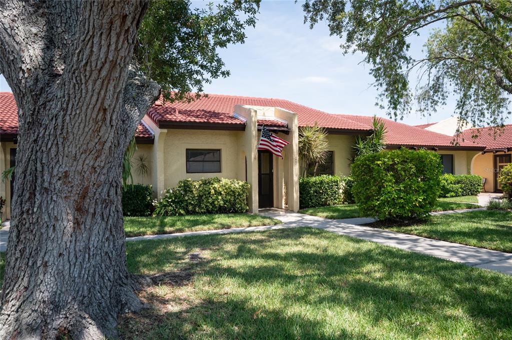 A single-story house with a red tile roof, beige stucco walls, and an American flag — 1407 58TH STREET W UNIT 1407, BRADENTON, FL