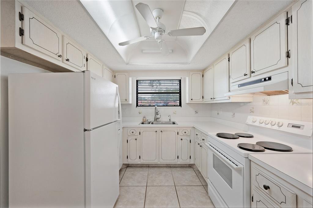 A white kitchen features tile flooring, a ceiling fan, and white cabinetry with black hardware — 1407 58TH STREET W UNIT 1407, BRADENTON, FL