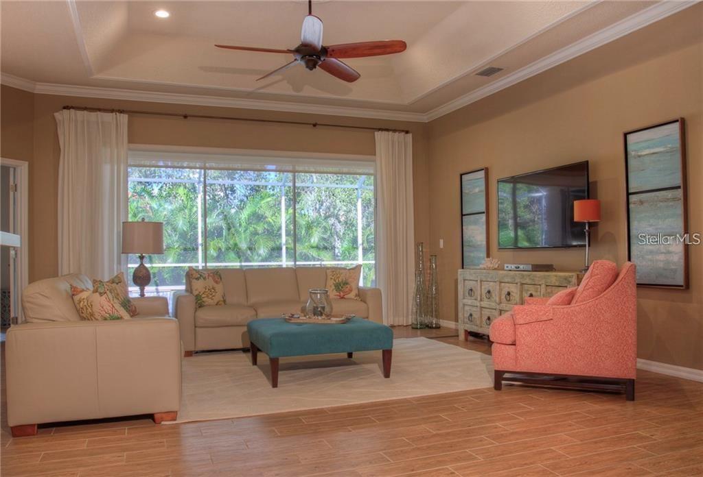 A living room features a tray ceiling, a large window, a sofa, and a coral armchair — 7348 STANHOPE COURT, SARASOTA, FL