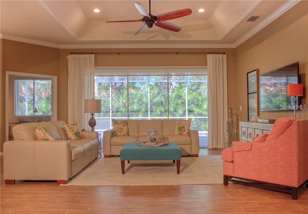 A living room features a tray ceiling, a teal ottoman, and a large sliding glass door — 7348 STANHOPE COURT, SARASOTA, FL
