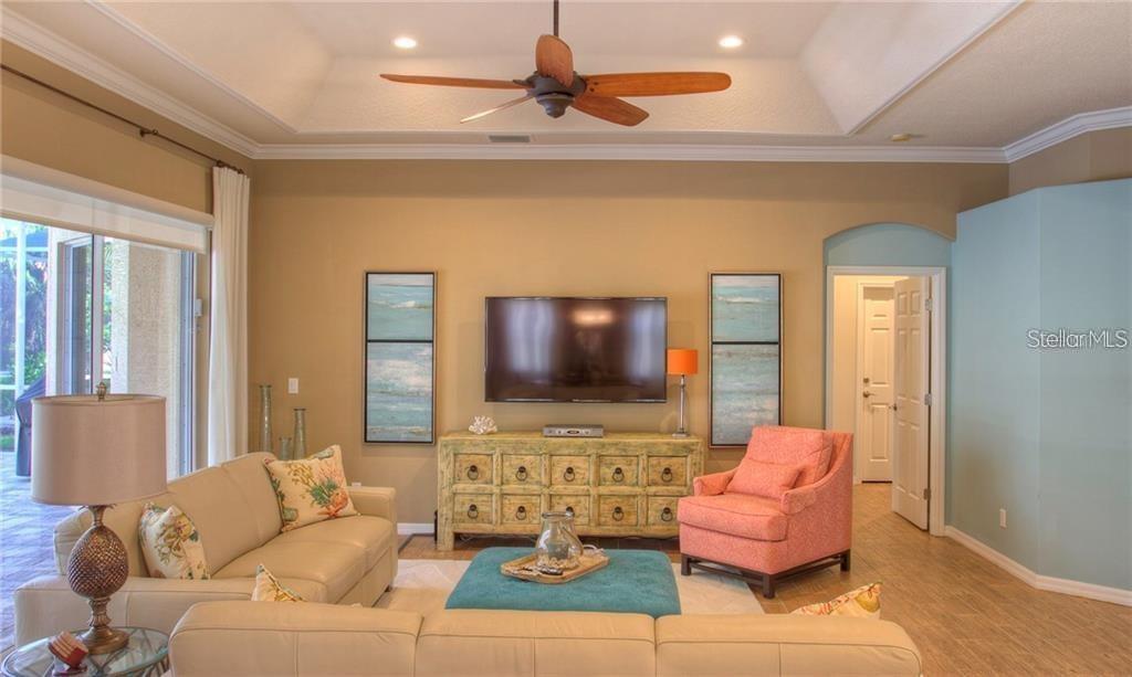 A living room features a beige sofa, a coral armchair, a teal ottoman, and a television — 7348 STANHOPE COURT, SARASOTA, FL