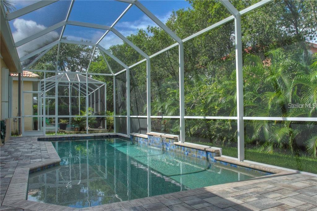 A swimming pool with a tiled water feature is enclosed by a white screen cage — 7348 STANHOPE COURT, SARASOTA, FL