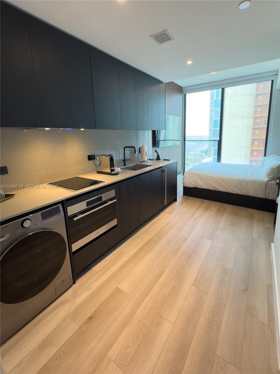 A modern studio apartment features a kitchenette with dark cabinets, stainless appliances, and a bed — 20 NE 11th St # 3006A, Miami FL 33132, MIAMI, FL