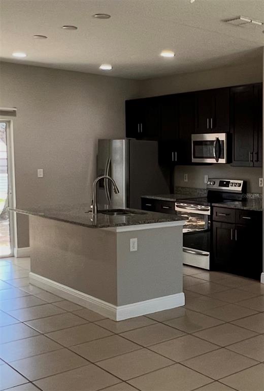 A kitchen features dark cabinetry, stainless steel appliances, a granite-topped island, and tile flooring — 528 FINCH LANE, KISSIMMEE, FL