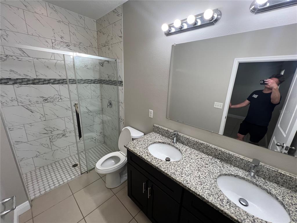 A bathroom features a double vanity with granite countertops, a toilet, and a tiled shower — 528 FINCH LANE, KISSIMMEE, FL