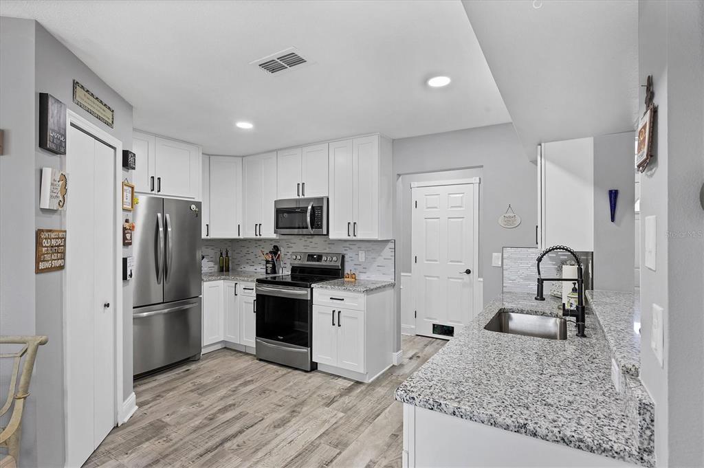 A kitchen with white cabinets, stainless steel appliances, granite countertops, and light wood-look flooring — 11302 3RD AVENUE E, BRADENTON, FL