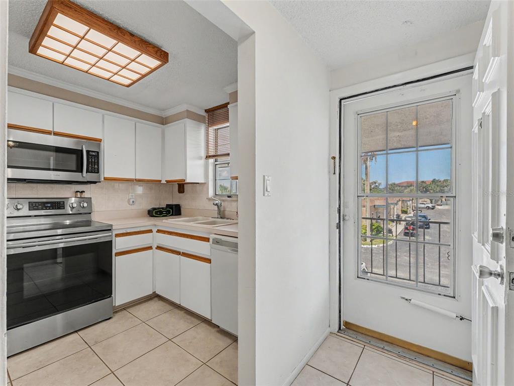 A kitchen with white cabinets and stainless steel appliances sits beside a glass-paned exterior door — 6340 E PROVIDENCE CIRCLE UNIT 204, NEW PORT RICHEY, FL
