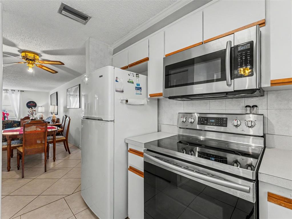 A kitchen features white cabinets, stainless steel appliances, and tile flooring, opening to a dining area — 6340 E PROVIDENCE CIRCLE UNIT 204, NEW PORT RICHEY, FL