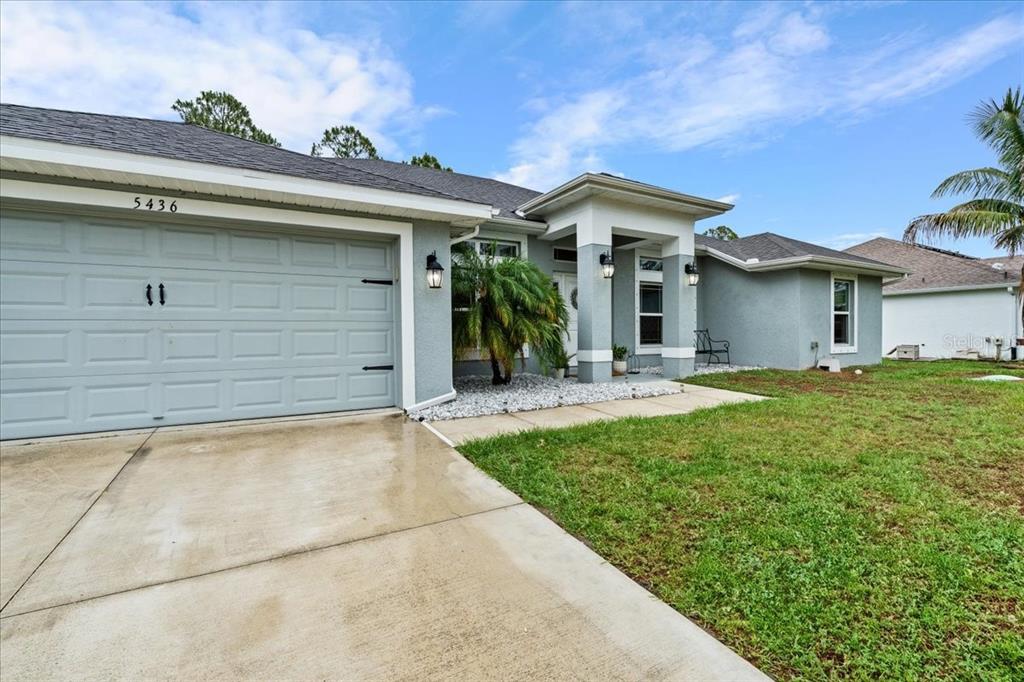 A single-story house with a gray stucco exterior, a two-car garage, and a covered entryway — 5436 JESSAMINE AVENUE, NORTH PORT, FL