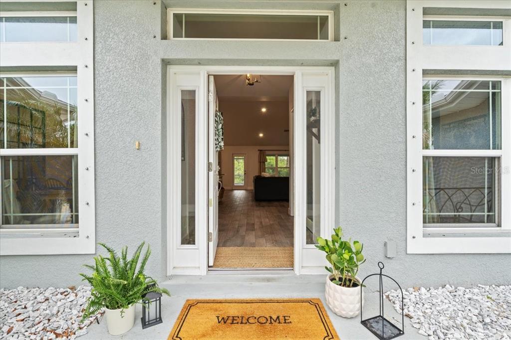 The front entrance of a house features a welcome mat, potted plants, and glass-paneled doors — 5436 JESSAMINE AVENUE, NORTH PORT, FL