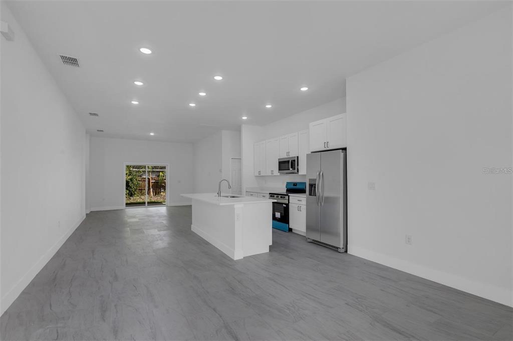 A modern kitchen with white cabinets and an island opens into a spacious living area — 1221 SW 5TH STREET, OCALA, FL