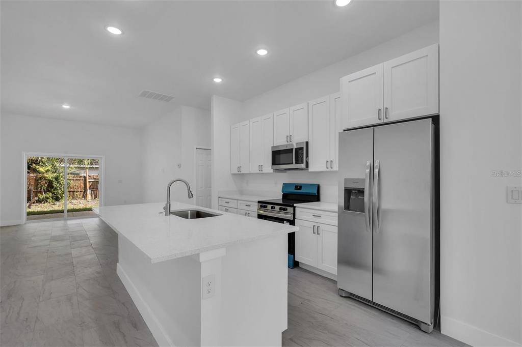 A modern kitchen features white cabinetry, stainless steel appliances, a quartz island, and tile flooring — 1221 SW 5TH STREET, OCALA, FL
