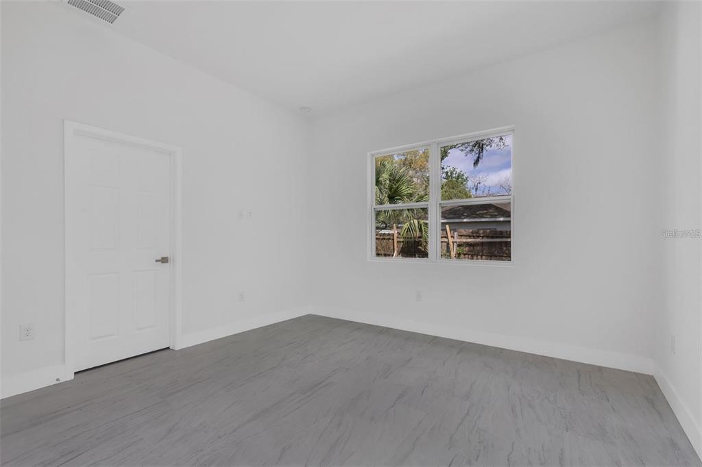 An empty bedroom with white walls, gray wood-look flooring, and a window overlooking a yard — 1221 SW 5TH STREET, OCALA, FL