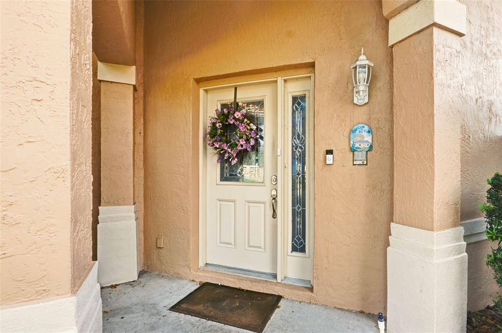 A beige front door with a floral wreath and sidelight sits under a covered entryway — 4870 WATERVISTA DRIVE, ORLANDO, FL
