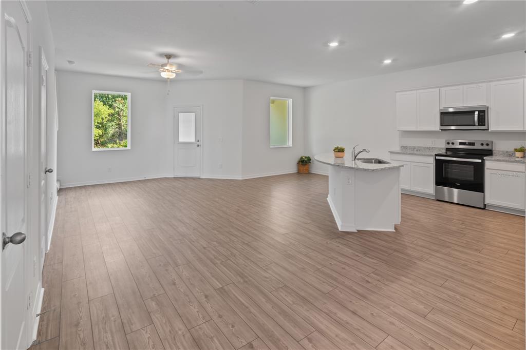 An open-concept kitchen and living area features white cabinets, stainless steel appliances, and wood-look flooring — 567 BAY LEAF DRIVE, KISSIMMEE, FL