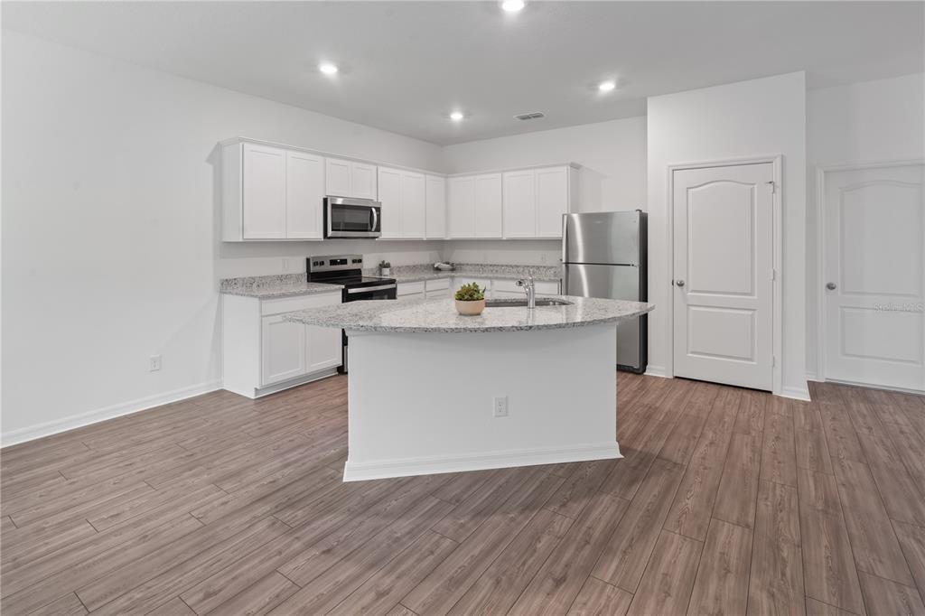 A kitchen features white cabinets, granite countertops, a central island, and wood-look flooring — 567 BAY LEAF DRIVE, KISSIMMEE, FL