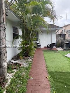 A brick walkway leads toward the side entrance of a white house with palm trees — 1074 NW 27th St # 0, Miami FL 33127, MIAMI, FL