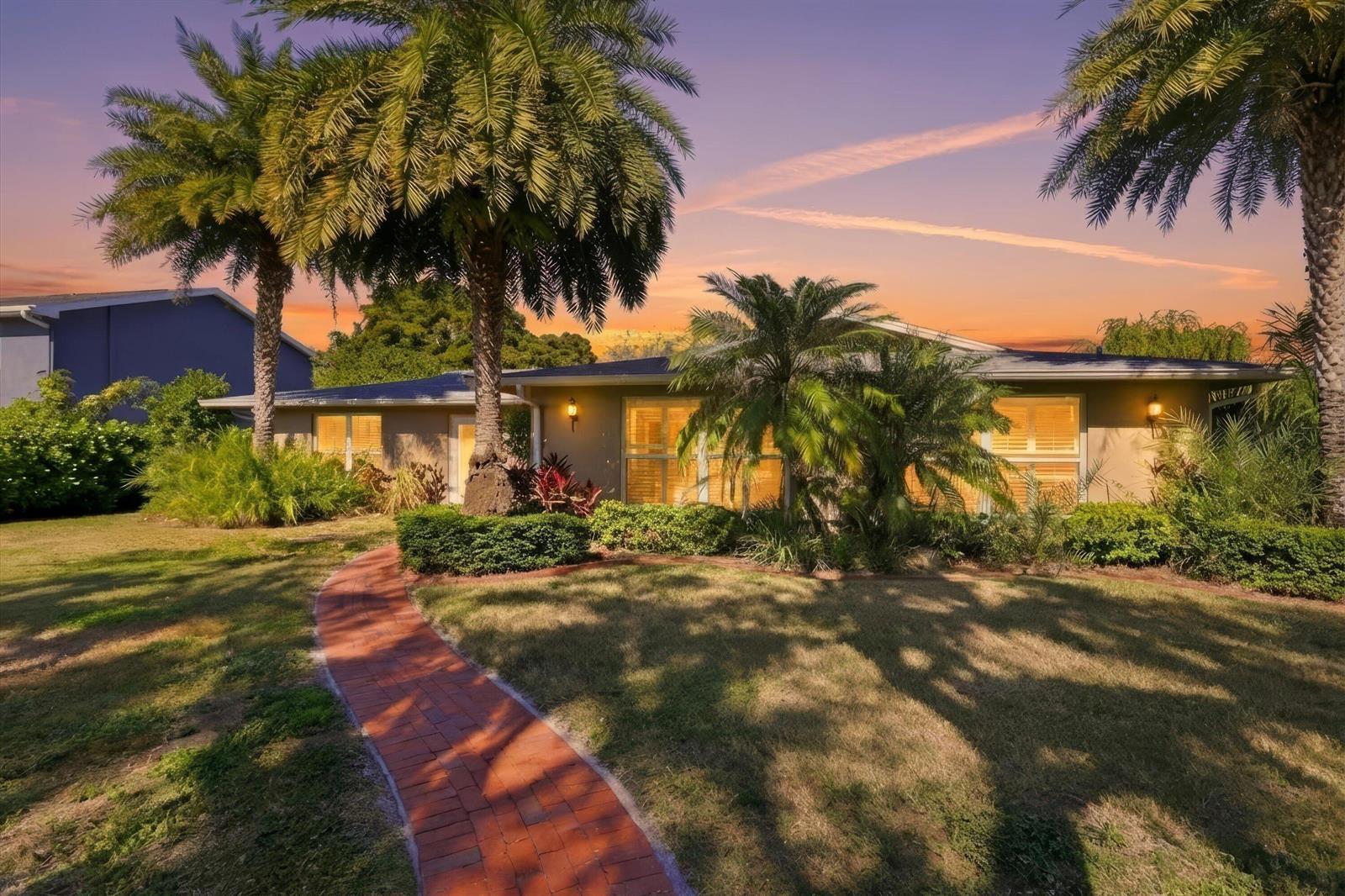 A single-story house with a brick walkway, palm trees, and a sunset sky — 74 Aqua Lane, FL 33903, FL