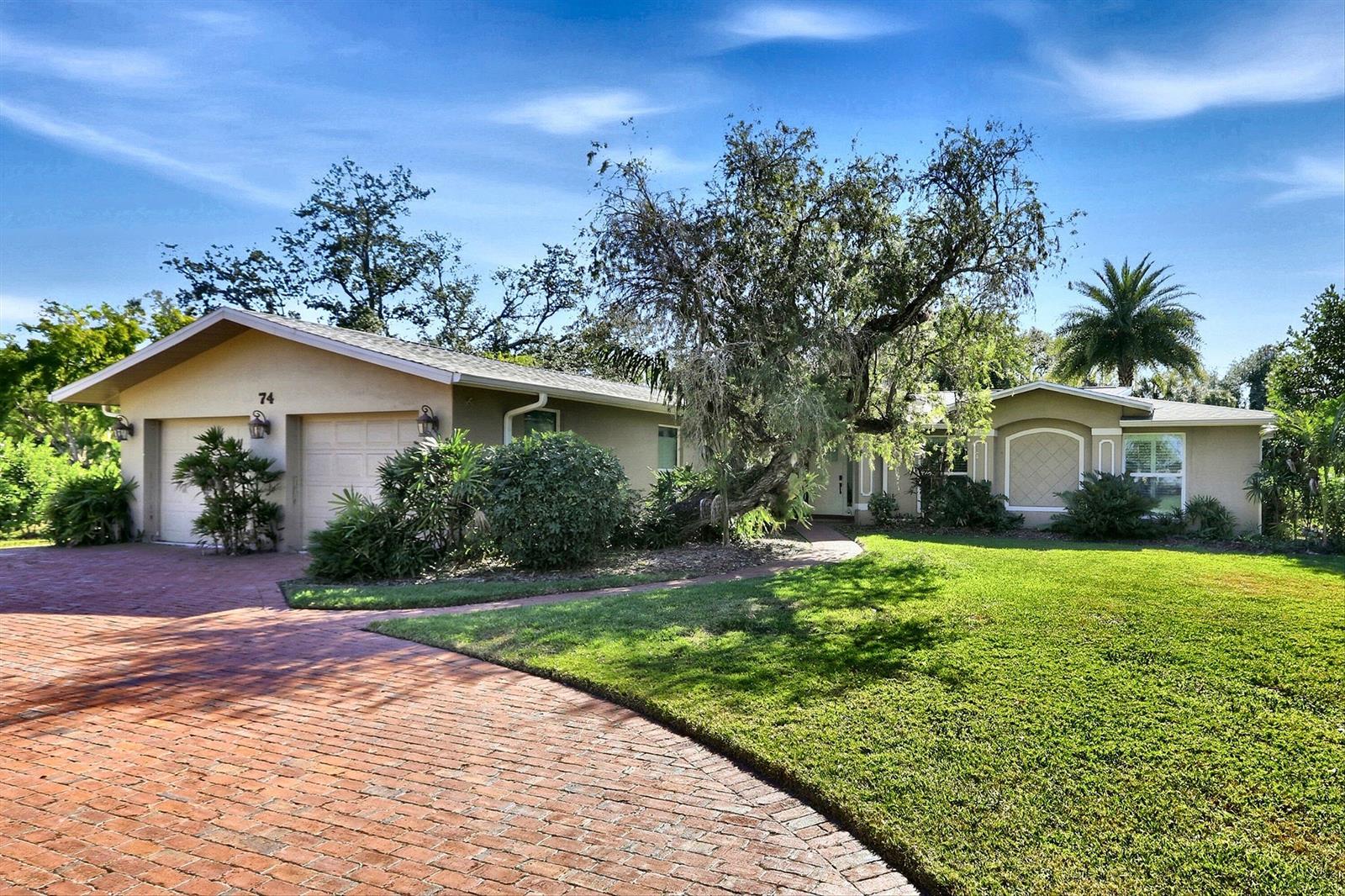 A single-story house with a brick driveway, a large tree, and a green lawn — 74 Aqua Lane, FL 33903, FL