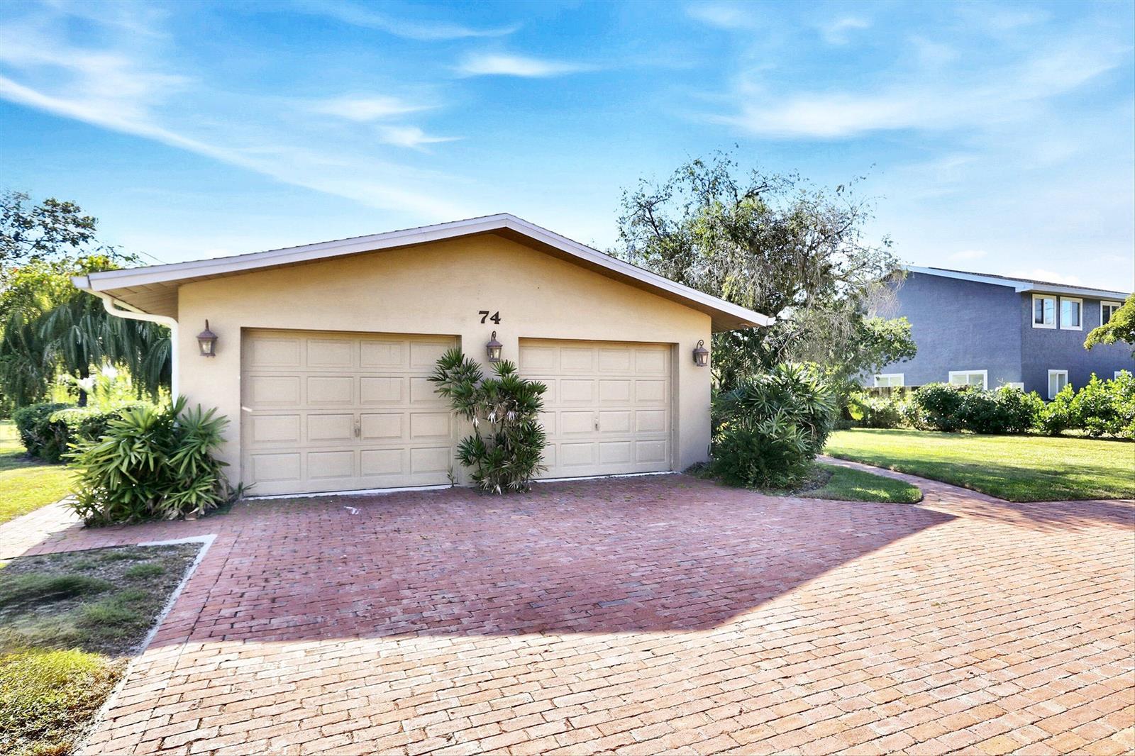 A tan two-car garage with a brick driveway and a number 74 above the doors — 74 Aqua Lane, FL 33903, FL