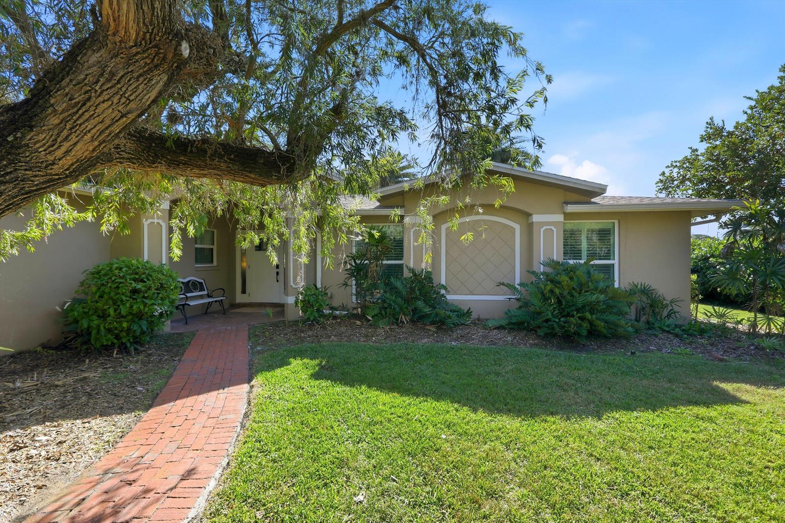 A brick walkway leads to the front entrance of a tan house with landscaping — 74 Aqua Lane, FL 33903, FL