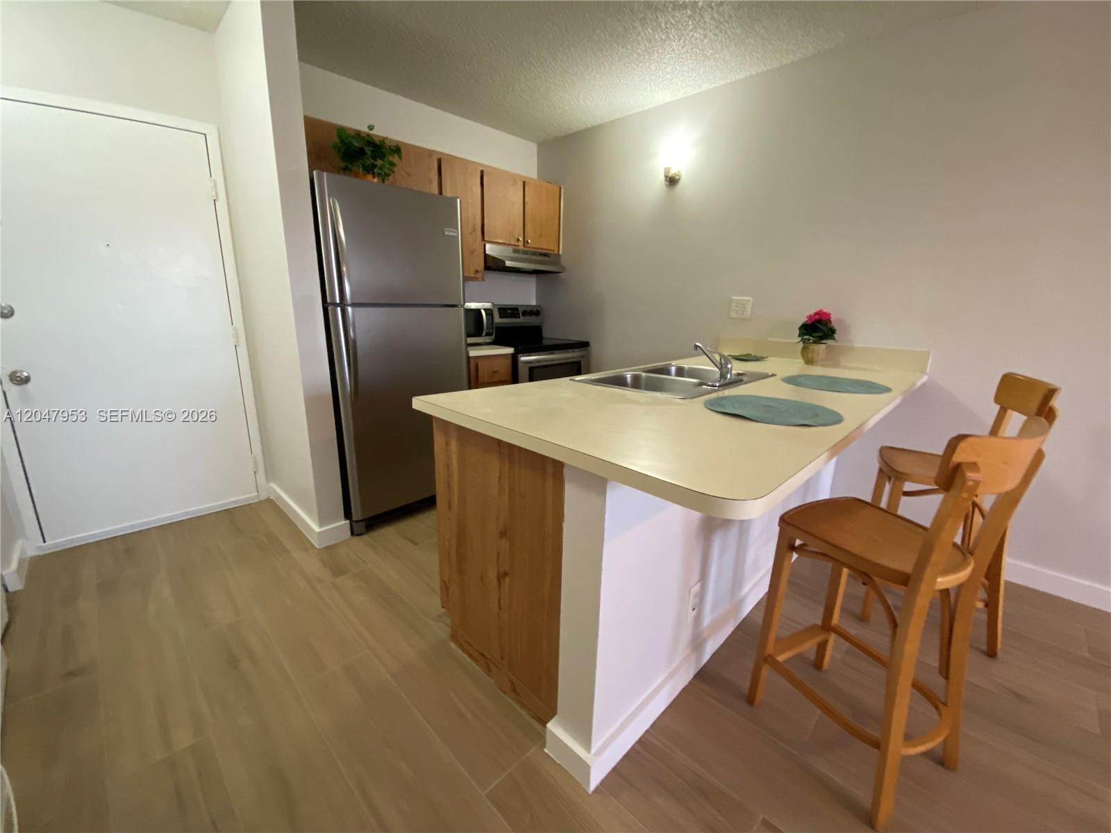 A kitchen features stainless steel appliances, wood cabinets, and a breakfast bar with two stools — CORAL SPRINGS, FL