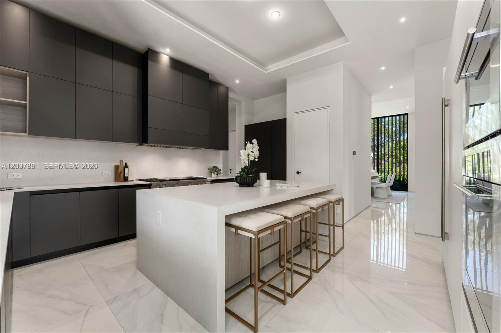 A modern kitchen features dark cabinetry, a white waterfall island, and light marble flooring — 4430 Nautilus Dr, Miami Beach FL 33140, MIAMI BEACH, FL