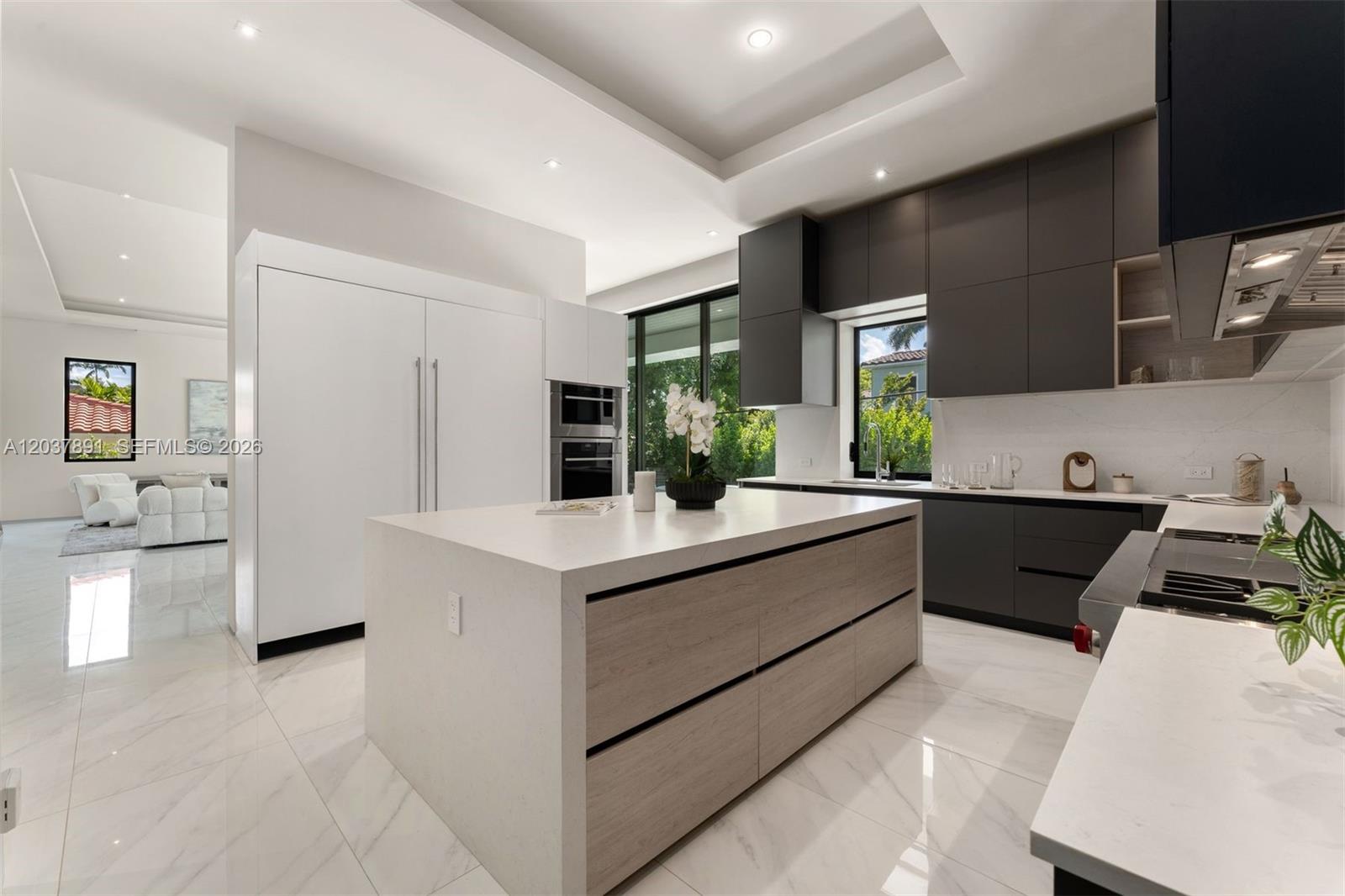 A modern kitchen features a large central island, dark cabinetry, and white marble-style flooring — 4430 Nautilus Dr, Miami Beach FL 33140, MIAMI BEACH, FL