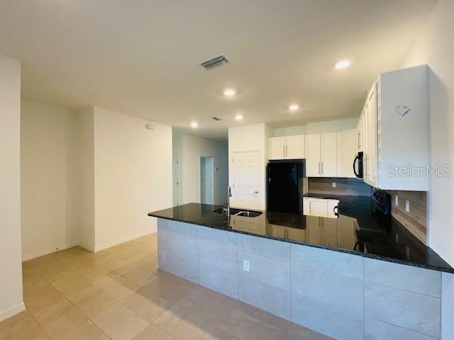 A kitchen features white cabinets, a black countertop island, and light-colored tile flooring — 15 CRABTREE COURT UNIT B, PALM COAST, FL