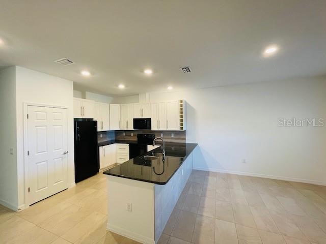 A modern kitchen features white cabinets, black appliances, and a dark granite-topped island — 15 CRABTREE COURT UNIT B, PALM COAST, FL