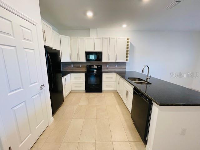 A kitchen features white cabinets, black appliances, and a dark granite island countertop — 15 CRABTREE COURT UNIT B, PALM COAST, FL