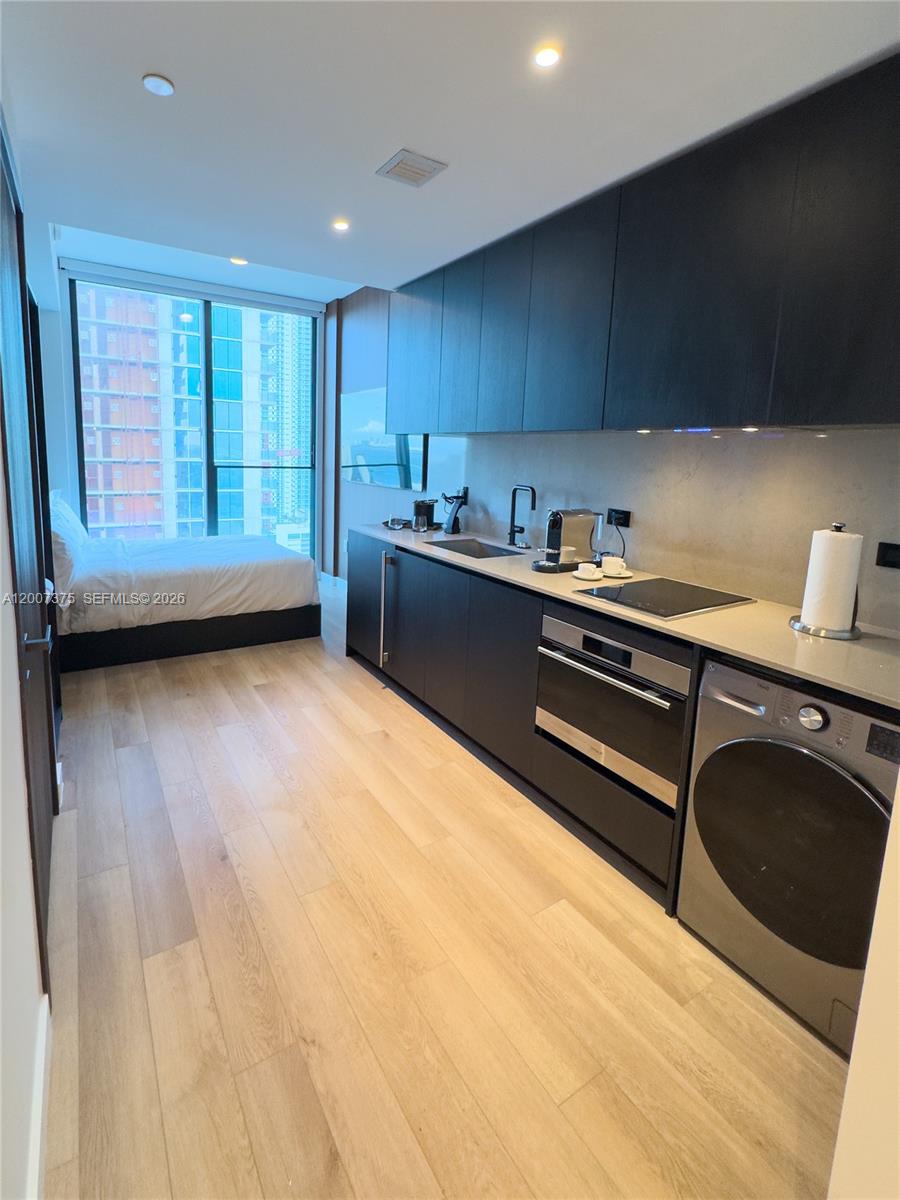 A studio apartment features a modern kitchenette with dark cabinetry and an adjacent bed — 20 NE 11th St # 3006B, Miami FL 33132, MIAMI, FL