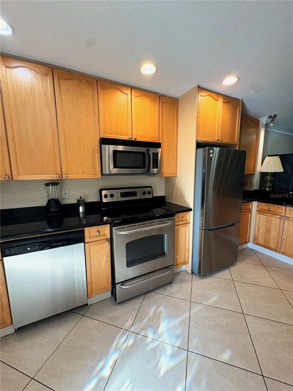 A kitchen features light wood cabinets, stainless steel appliances, black countertops, and tiled flooring — 11605 3RD STREET E UNIT 306, TREASURE ISLAND, FL