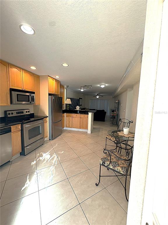 A kitchen with light wood cabinets, stainless steel appliances, and tile flooring opens to a living area — 11605 3RD STREET E UNIT 306, TREASURE ISLAND, FL