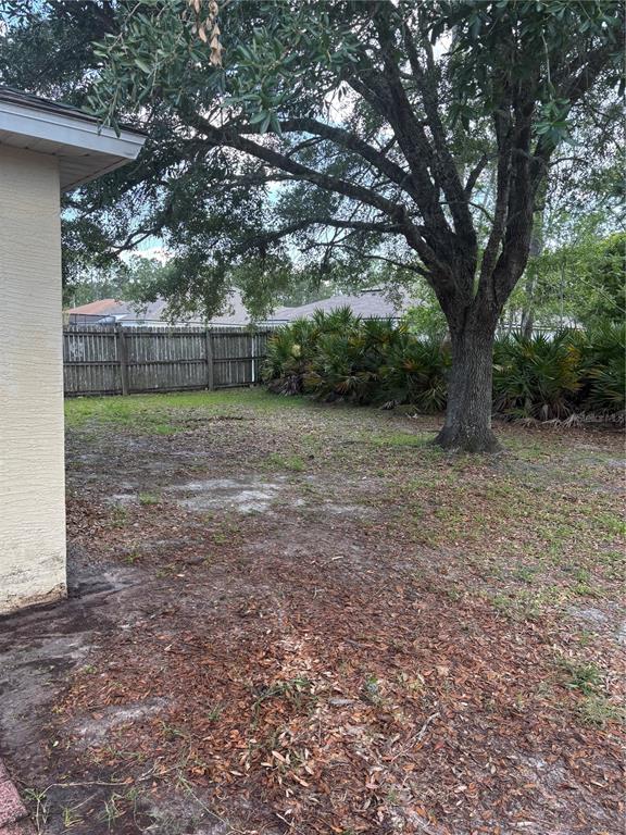 A backyard features a large tree, a wooden fence, and patches of grass and dirt — 18 RED CLOVER LANE, PALM COAST, FL