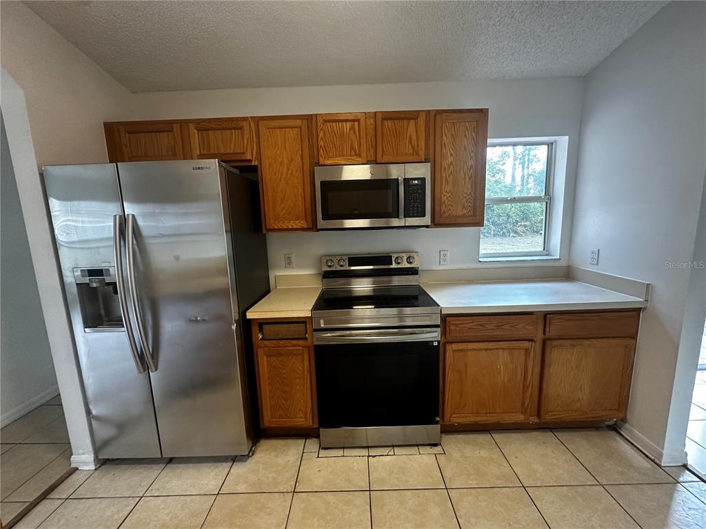 A kitchen features oak cabinets, stainless steel appliances, white countertops, and light-colored tile flooring — 18 RED CLOVER LANE, PALM COAST, FL