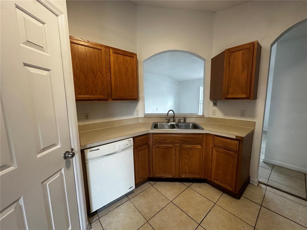 A kitchen features oak cabinets, a white dishwasher, a double sink, and beige tile flooring — 18 RED CLOVER LANE, PALM COAST, FL