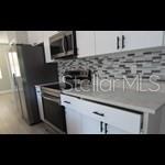 A kitchen features white cabinets, stainless steel appliances, and a gray patterned tile backsplash — 179 FISHER WAY TRAIL, OCKLAWAHA, FL