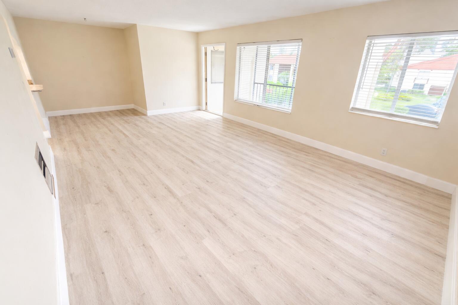 An empty living room with light wood-look flooring, beige walls, and two windows — 4759 Sable Pine Circle # A2, West Palm Beach FL 33417, WEST PALM BEACH, FL