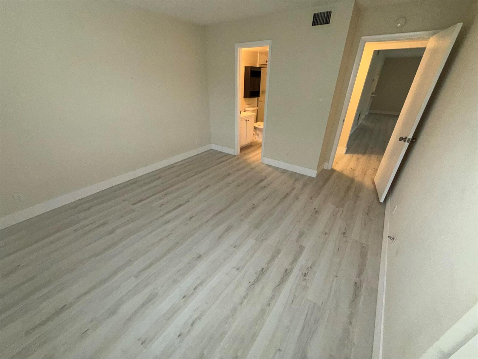 An empty room features light-colored wood-look flooring, beige walls, and two open doorways — 4759 Sable Pine Circle # A2, West Palm Beach FL 33417, WEST PALM BEACH, FL