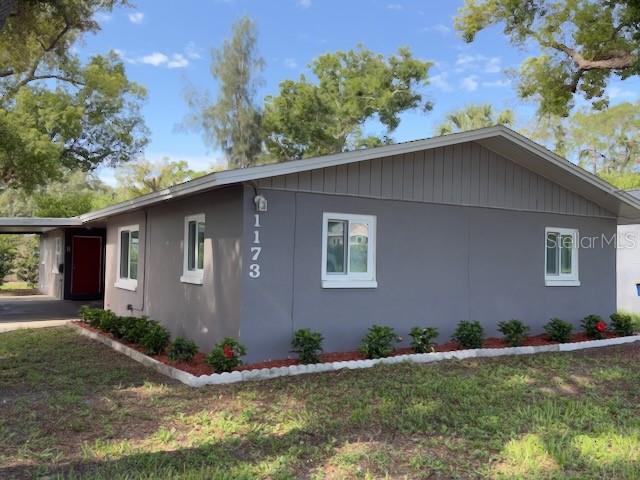 A gray single-story house features a carport, white-trimmed windows, and a landscaped front garden — 1173 GRANADA STREET, CLEARWATER, FL
