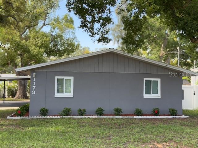 A gray, single-story house exterior features white-trimmed windows and a small landscaped garden bed — 1173 GRANADA STREET, CLEARWATER, FL