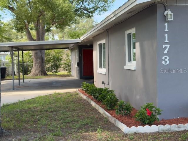 A gray house exterior features a red front door, a carport, and a landscaped garden bed — 1173 GRANADA STREET, CLEARWATER, FL
