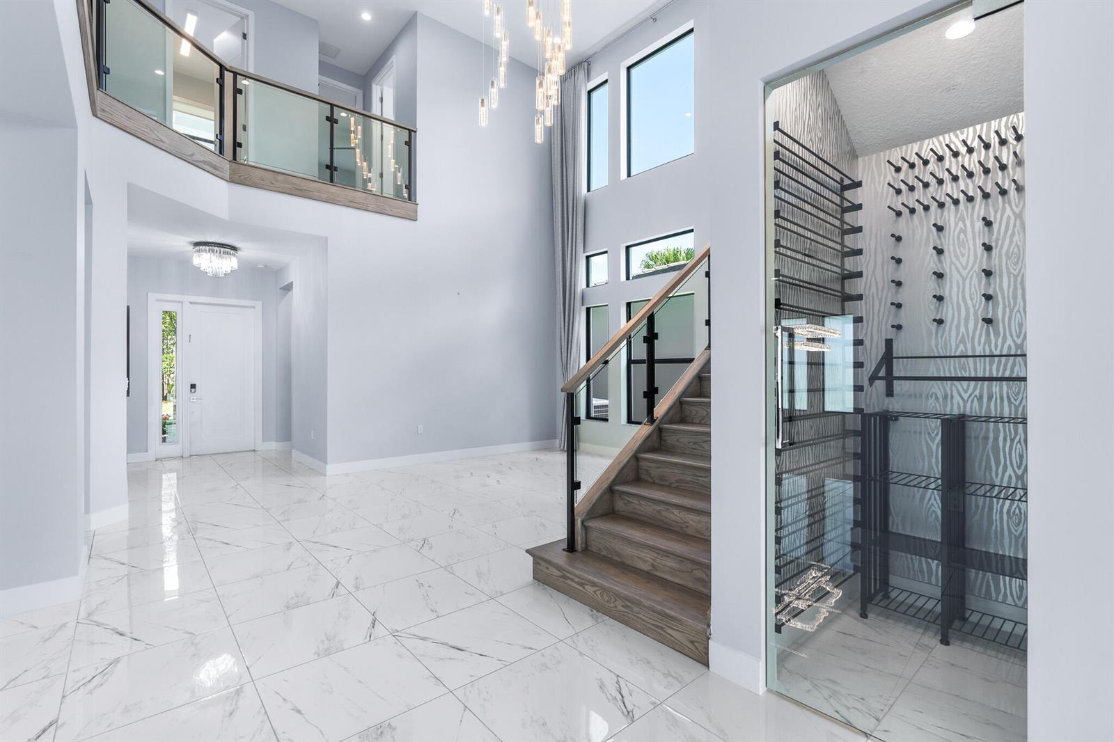 A modern, two-story living area features marble floors, a glass-enclosed wine cellar, and a staircase — 17411 Sea Blossom Way, Boca Raton FL 33496, BOCA RATON, FL