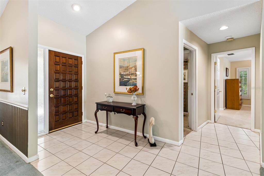 A tiled entryway features a wooden front door, a console table, and a vaulted ceiling — 5804 AINSWORTH COURT E, TAMPA, FL