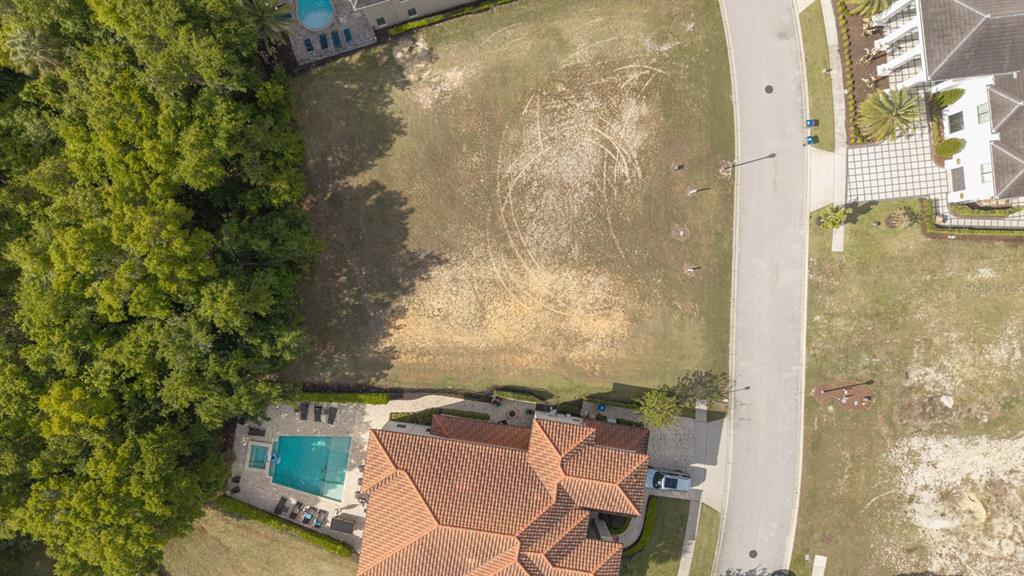 An aerial view shows a vacant residential lot situated between two houses and a wooded area — 8188 VALHALLA TERRACE, REUNION, FL